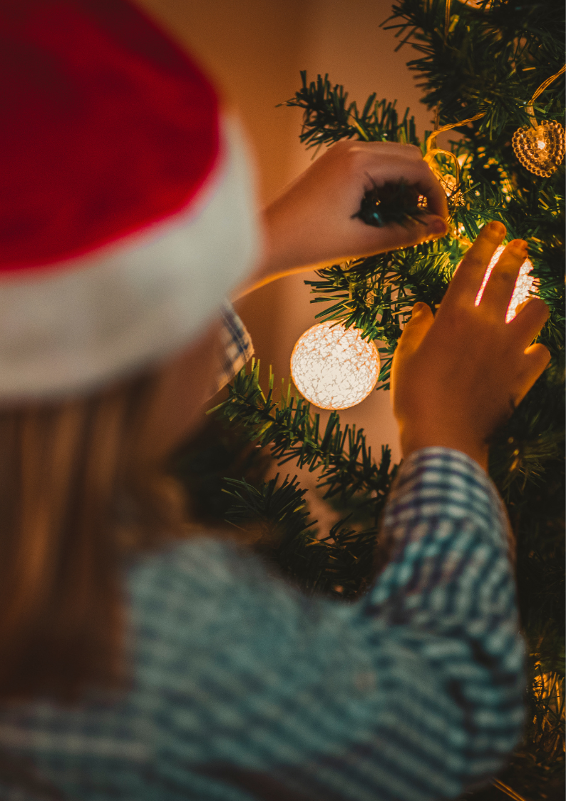 Bambina che appende una pallina sull'albero di Natale con cappello di Babbo Natale