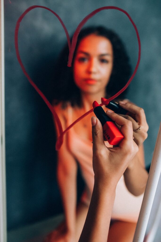 donna che disegna un cuore allo specchio con il rossetto rosso